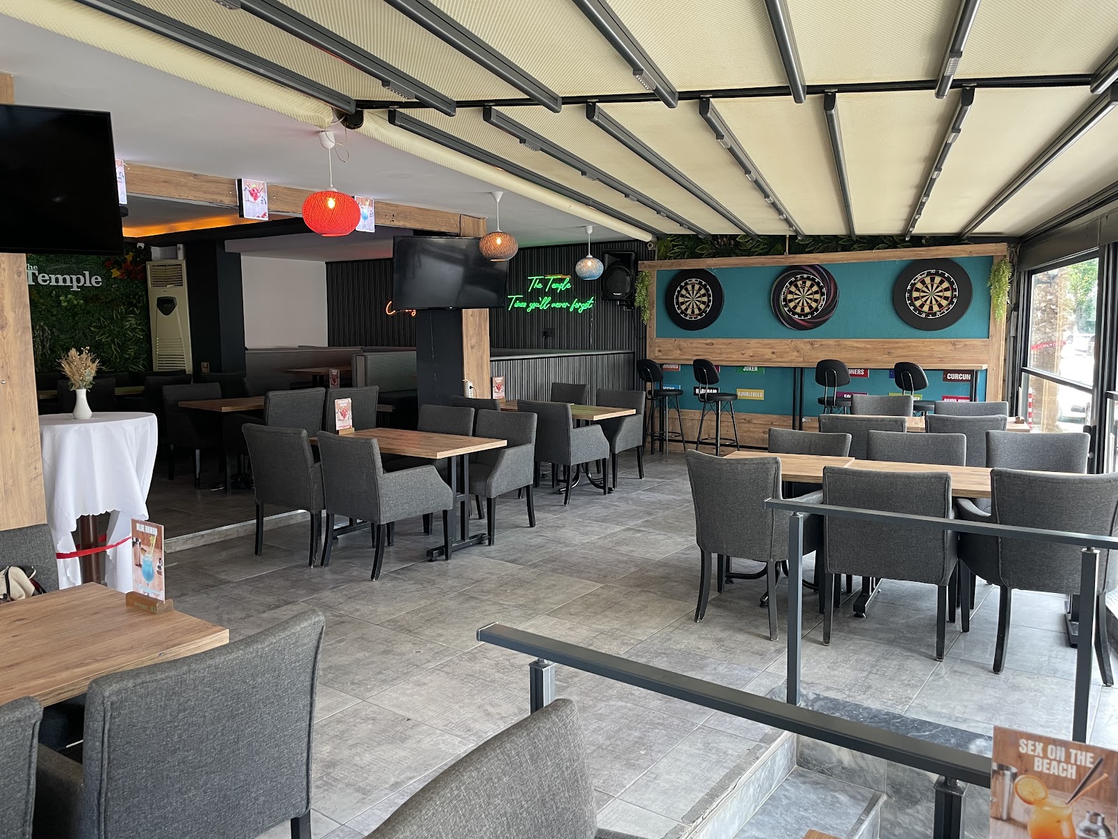 The Temple’s covered terrace with grey chairs, wooden tables and two dartboards on a teal wall