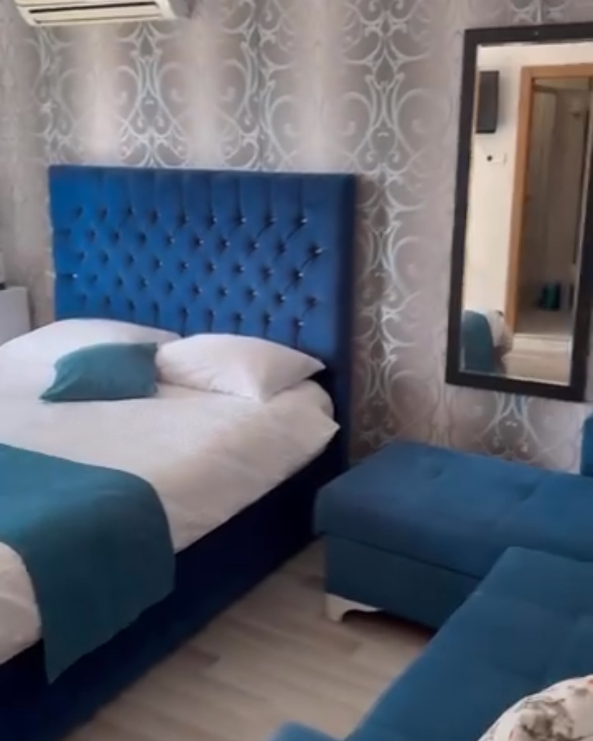 Room with a royal blue tufted headboard, matching blue sofa and a tall mirror