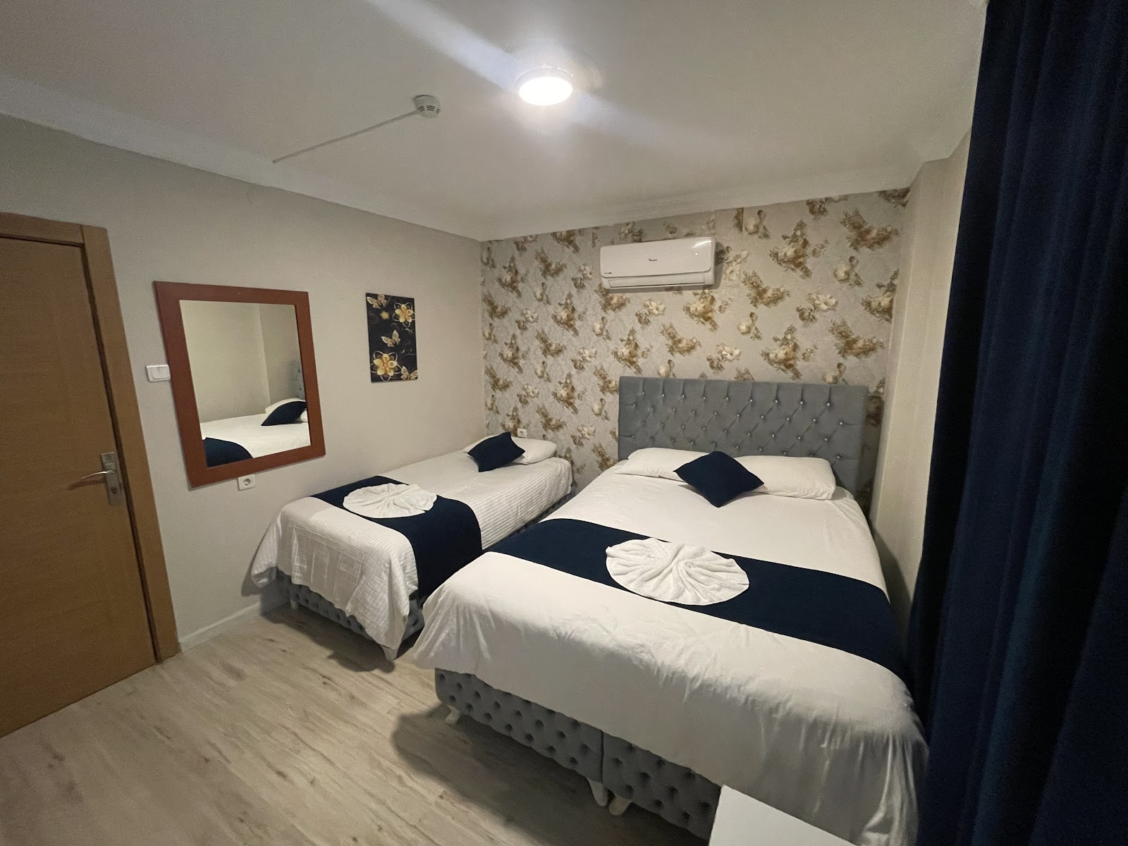 Room with a double bed and a single bed, navy throws, folded towels and patterned wallpaper