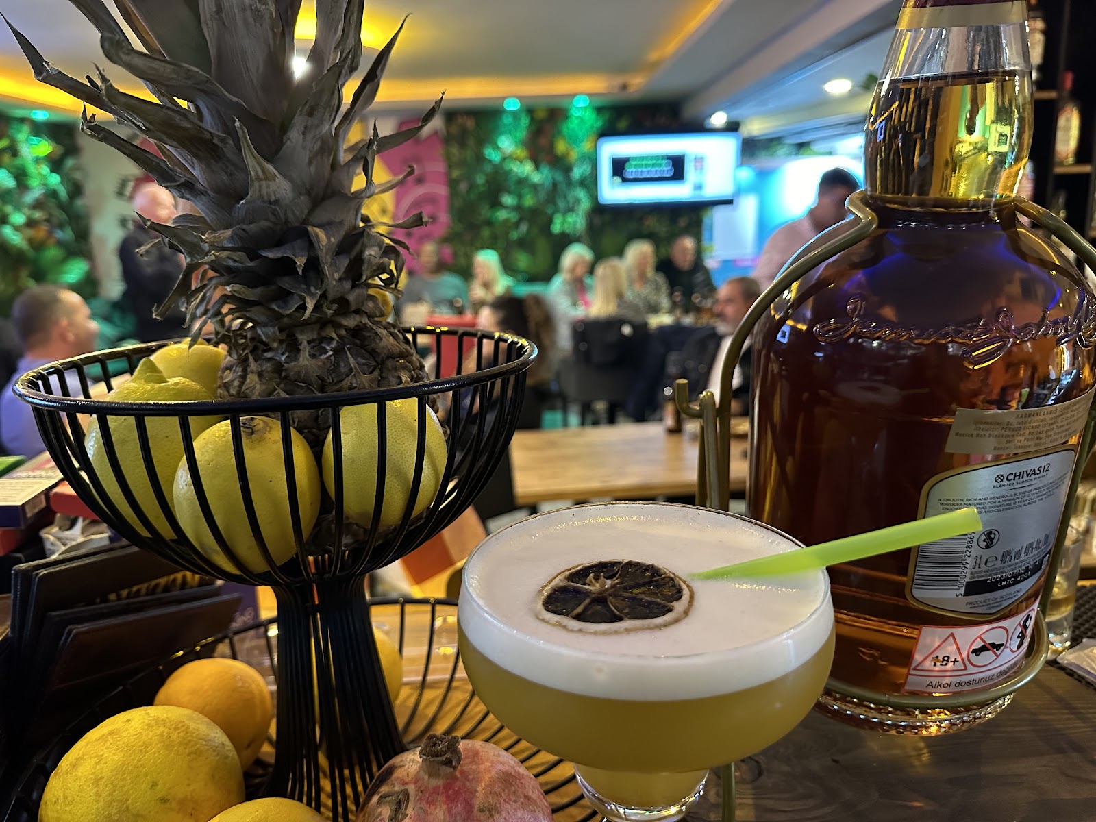 Foamy sour cocktail with a dried lemon wheel next to a fruit bowl